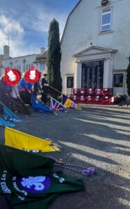 red poppy wreaths laid in front of war memorial with lowered flags in foreground