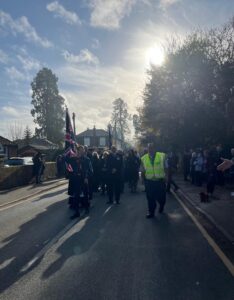 parade of people marching along road with boy scout holding flag at the front
