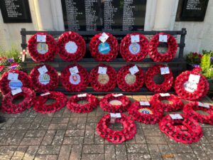 Red poppy wreaths laid in front of stone war memorial with names engraved