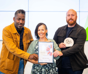 man with yellow jacket, lady and flower blouse and man in black jacket holding certificate