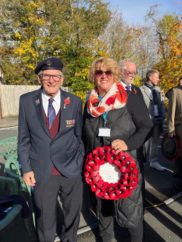 male war veteran in suit wearing beret and medals with female chairperson holding poppy wreath