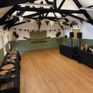 An AI-generated image of a hall room with 50th birthday banners, black and gold balloons and food on tables