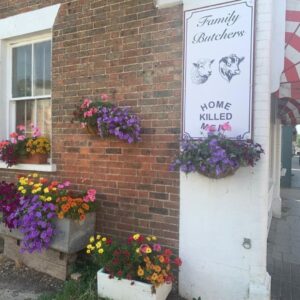 Brick shop wall with flower planters and family butcher sign