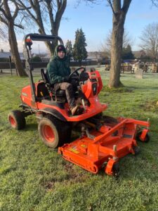 groundsman on orange mower cutting grass in cemetery